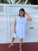 Vestido corto blanco de lino 100%, fabricado en Italia, con volados en las mangas y el ruedo inferior, y botones de nácar.