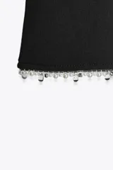 Pantalón negro de tiro alto, corte ajustado y cintura elástica. El ruedo es acampanado y está decorado con perlas.
