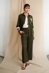 Camisa verde militar de manga larga con puños color crema, cuello clásico y cierre frontal con botones. Tiene un bolsillo en el pecho con bordado de una palmera color crema.