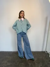 Camisa de popelina a rayas verticales verdes y blancas, con cuello rosa y botones marmolados. Es más corta adelante y más larga atrás.
