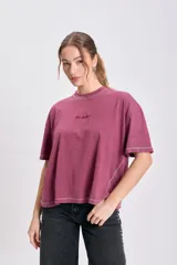 Remera de manga corta color bordó con efecto lavado, corte holgado y costuras externas visibles en blanco en cuello, mangas y ruedo. Presenta un pequeño bordado cursivo en el pecho.
