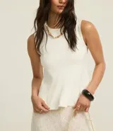 Blusa sin mangas color blanco, confeccionada en punto roma, con cuello redondo y corte peplum.