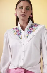 Camisa blanca de manga larga con cuello mao, bordado floral en el pecho, abertura triangular y volantes.