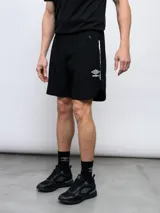 Short deportivo negro de poliéster y spandex, con cintura elástica, bolsillos laterales con cierre y logo de Umbro estampado en blanco.