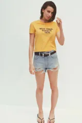 Camiseta amarilla de algodón con cuello redondo, manga corta y estampado marrón con el texto "New York Fluxus 1970".