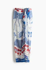 Pareo rectangular de tejido liviano con estampado de motivos marinos, botellas, frutas y rayas en tonos rojo, azul y blanco.