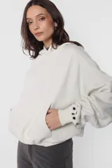Buzo tipo hoodie color beige, de frisa gamuzada, con silueta oversize, bolsillo canguro, puños y cintura de ribb, capucha forrada con jersey y aplique de ojalillos en los puños.