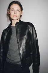 Chaqueta bomber de cuero negra con cuello alto, cierre frontal con cremallera, bolsillos laterales y puños y bajo elásticos.