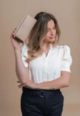 Billetera color beige con doble compartimento con cierre, correa de mano y logo de la marca en el frente.