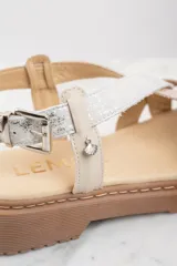 Sandalias con plataforma color beige y suela marrón. Tiras cruzadas en cuero color beige con textura y cuero plateado brillante.