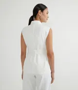 Chaleco blanco en sarga con cuello solapa, cierre en botones, martingale en el hombro, cuatro bolsillos delanteros con solapa, cintura con transeúntes anchos y cinturón con pespuntes para amarre.