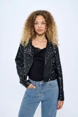 Chaqueta corta estilo motoquera de cuero sintético negro, con cuello solapa y cierre cruzado con cremallera. Decorada con tachas plateadas en solapas, hombros y mangas.