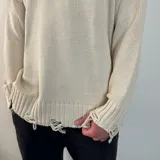 Sweater tejido color crema con cuello redondo y terminaciones con efecto desgastado y roturas.