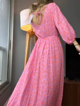Vestido largo de tela estampada en tonos rosa, naranja y lila, con escote en V en la espalda que se ata con lazos.