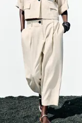 Pantalón color crema de tiro alto con pinzas delanteras y cintura elástica en la espalda. Tiene bolsillos delanteros y traseros.