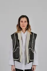 Chaleco reversible confeccionado en lambskin, con una cara de cuero en color marrón oscuro y otra de lana blanca. Presenta bolsillos frontales aplicados con ribetes de lana en contraste y diseño de cuello abierto.