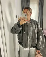 Campera bomber gris con diseño acolchado, cierre frontal con cremallera y broches a presión, cuello, puños y bajo acanalados.