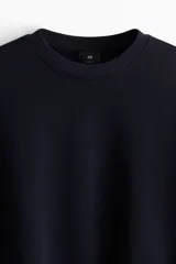 Buzo azul marino de tejido de mezcla de algodón de peso medio con interior cepillado suave. Modelo con cuello redondo ribeteado, hombros caídos y remate acanalado ancho en puños y bajo. Corte holgado.