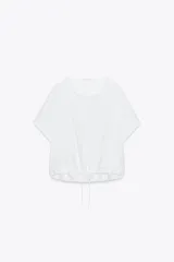 Camiseta blanca de algodón con cuello redondo, mangas cortas y bajo asimétrico ajustable con lazadas.