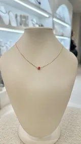 Collar dorado con dije cilíndrico rojo.