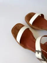 Sandalias de cuero color crudo, con dos tiras anchas sobre el empeine, pulsera al tobillo con hebilla y taco cuadrado de madera.