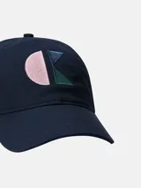 Gorra de béisbol de seis paneles, color azul marino, con visera curva y cierre ajustable. Presenta un monograma bordado en la parte frontal compuesto por formas geométricas en tonos rosa pálido, azul claro y verde esmeralda.