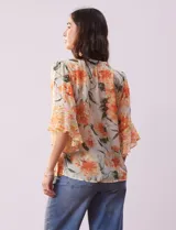 Blusa de gasa estampada con flores color naranja, marca Figueroa & Flower. Tiene cuello a la base, escote en V con lazo, abertura central con botones, delantera plisada y mangas 3/4 amplias.