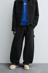 Pantalón negro de corte amplio, confeccionado en tejido de algodón con efecto lavado. Presenta bolsillos frontales, traseros de parche, tira multifunción y bolsillos laterales en las perneras. Cuenta con cierre frontal con cremallera y botón.