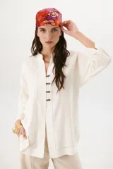 Sobrecamisa beige de corte recto, cuello mao y mangas 3/4. Presenta cierre frontal con botones de madera y bolsillos laterales.