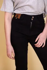 Pantalón jean negro de tiro alto, con cinco bolsillos, confeccionado en tela con elastano. Tiene cierre frontal con doble botón y cierre metálico, y detalle de cuero en la parte delantera de la pretina.