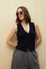 Chaleco tejido color blanco, con escote en V profundo y cierre frontal de botones a tono. Presenta una trama acanalada y corte ajustado al cuerpo.