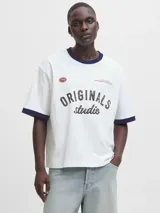 Remera blanca de manga corta y cuello redondo, con fit oversize y largo cropped. Tiene ribetes azul marino en el cuello y las mangas. Estampado frontal con la palabra "ORIGINALS" en negro y "studio" en cursiva, junto a detalles en rojo como "1990" y "COPENHAGEN CREATIVE DEPT.".