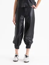 Pantalón Frey de cuero ovino color negro, con frunces en el puño de la botamanga que aportan volumen. Tiene cintura doble con pespunte y botones forrados en cuero.