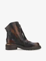 Bota corta de cuero bovino con efecto envejecido en tonos marrón oscuro y caramelo. Presenta cierre frontal con cremallera y suela de goma gruesa con relieve. El tacón bajo tiene un detalle metálico horizontal en color cobre.