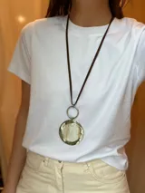 Collar largo con colgante circular de guampa engarzado en alpaca plateada, con aros de acero y tiento marrón. Se cierra con cadena de acero quirúrgico con mosquetón para regular el largo.