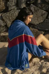 Hoodie azul de toalla con capucha, mangas largas y diseño color block con franja roja y ribete amarillo en el pecho. Logotipo bordado en el frente y bolsillos laterales.