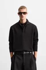 Polo de manga larga color negro, de punto tejido en hilatura de algodón, corte relaxed fit, con cuello solapa y cierre frontal de botonadura.