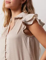 Camisa color beige de satén, con cuello con solapa y escote en V. Tiene una apertura central con botones y sisas con volados.