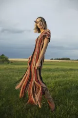 Vestido corto tejido a crochet con lurex, con escote en V y mangas cortas. Diseño a rayas horizontales en tonos naranja, marrón y negro, con flecos en el ruedo.