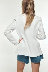 Blazer color blanco hueso, de corte entallado y doble botonadura dorada. Tiene cuello con solapa, mangas largas con hombreras y bolsillos delanteros con solapa.