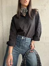 Camisa negra con bordados florales en las mangas, cuello clásico y cierre frontal con botones.