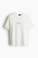 Remera blanca de corte holgado con estampado de texto en cursiva color negro en el centro del pecho.