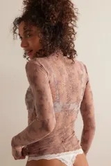 Top de manga larga, cuello alto y calce ajustado, confeccionado en tul negro transparente con estampado floral en gris. Presenta aberturas para los pulgares en los puños.