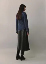 Camisa de denim azul oscuro con cuello camisero, cierre frontal con botones a presión, dos bolsillos con solapa abotonada en el pecho y mangas largas con puños abotonados. Incluye bolo tie con dije plateado y turquesa.
