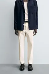 Pantalón chino negro de corte relajado (relaxed fit) con tiro medio, confeccionado en algodón con elasticidad. Presenta bolsillos delanteros y bolsillos traseros de vivo, con cierre frontal de cremallera y botón.