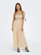 Vestido midi color crema, con tirantes finos ajustables, escote recto y cuerpo fruncido con detalle de borlas negras.