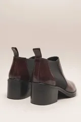 Botín negro de cuero vacuno con acabado charol, estilo botín Chelsea con puntera fina y elástico lateral. Posee un taco ancho y bajo de 5.5 cm.