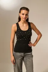 Musculosa negra de bretel fino, con cuello redondo profundo y diseño ajustado al cuerpo. Presenta detalles de studs y strass en la parte frontal.