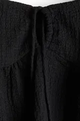 Top corto negro en punto arrugado con escote corazón, manga circular y sección cut-out con cordón para ajustar en el busto. Modelo ajustado sobre el busto con copas preformadas fruncidas y peplum con leve vuelo.
