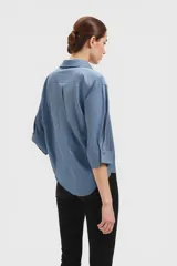 Camisa celeste de corte holgado con cuello clásico, cierre frontal con botones y mangas 3/4 con puños.